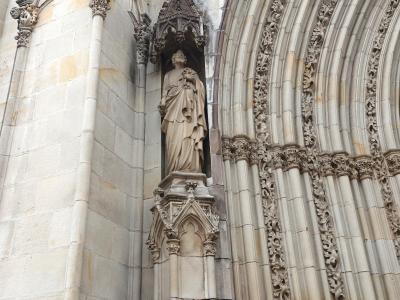 A close-up view of Gothic stone architecture featuring a statue in a niche, a gargoyle, and an ornate arched doorway.