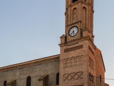 A brick church with a tall, octagonal bell tower featuring a clock and a cross, set against a clear sky.