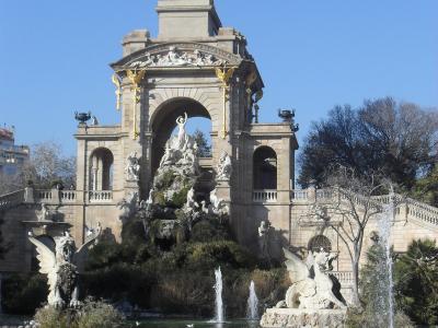 The image shows the Font de la Cascada (Cascade Fountain) within the Parc de la Ciutadella in Barcelona, featuring a large triumphal arch topped with a golden quadriga sculpture and surrounded by fountains and statues.