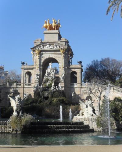 The image shows the Font de la Cascada (Cascade Fountain) within the Parc de la Ciutadella in Barcelona, featuring a large triumphal arch topped with a golden quadriga sculpture and surrounded by fountains and statues.