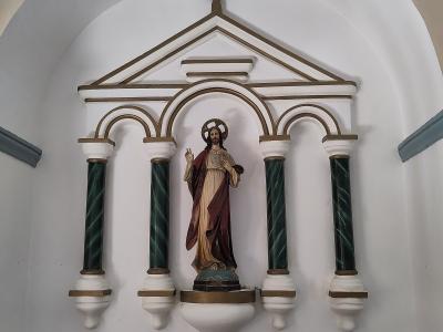 The image shows an interior religious niche containing a statue of Jesus Christ (Sacred Heart) set within a white and gold architectural structure with green marbleized columns, located inside a church.