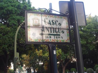 A decorative street sign mounted on a black metal pole, displaying the text "CASCO ANTIGUO" and "OLD TOWN" with an arrow pointing left, alongside a coat of arms emblem.