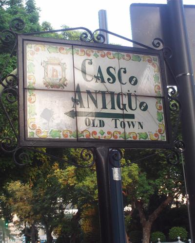 A decorative street sign mounted on a black metal pole, displaying the text "CASCO ANTIGUO" and "OLD TOWN" with an arrow pointing left, alongside a coat of arms emblem.