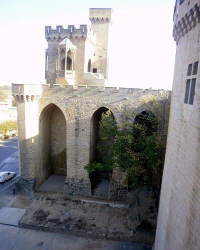 A high-angle view of the exterior stone walls, arched gateways, and a crenellated tower of the Royal Palace of Olite, with a street and white van visible below.