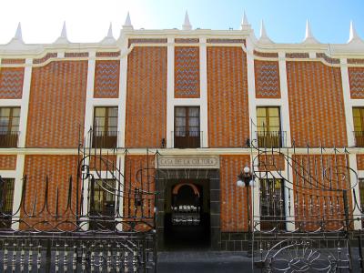 A two-story building with a distinctive orange and white patterned tile facade, white architectural trim, and a central entrance gate with a sign reading "CASA DE LA CULTURA".