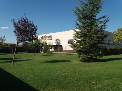 A white building with a large sign reading "DINÓPOLIS" and "TIERRA ABRIGADA" on its facade, set against a blue sky with green grass and trees in the foreground.