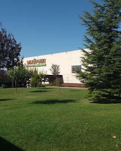 A white building with a large sign reading "DINÓPOLIS" and "TIERRA ABRIGADA" on its facade, set against a blue sky with green grass and trees in the foreground.