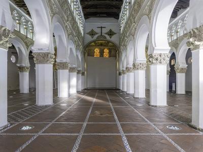 A panoramic interior view of a large hall featuring rows of white octagonal columns supporting double-tiered horseshoe arches with ornate capitals, leading to an apse with a Christian cross and iconography.