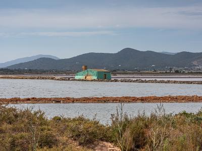 A landscape view of salt evaporation ponds with a small green building in the middle ground and hills in the background.