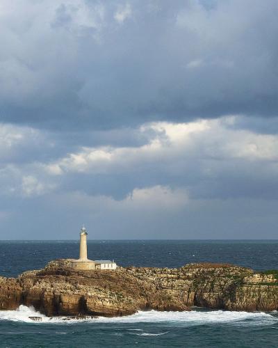 A conical white lighthouse situated on a small, rocky island surrounded by the sea under a cloudy sky.