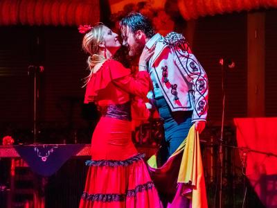 A male and female flamenco dancer performing on a stage with red lighting and Moorish-style arches in the background.