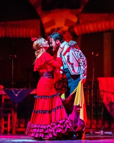 A male and female flamenco dancer performing on a stage with red lighting and Moorish-style arches in the background.