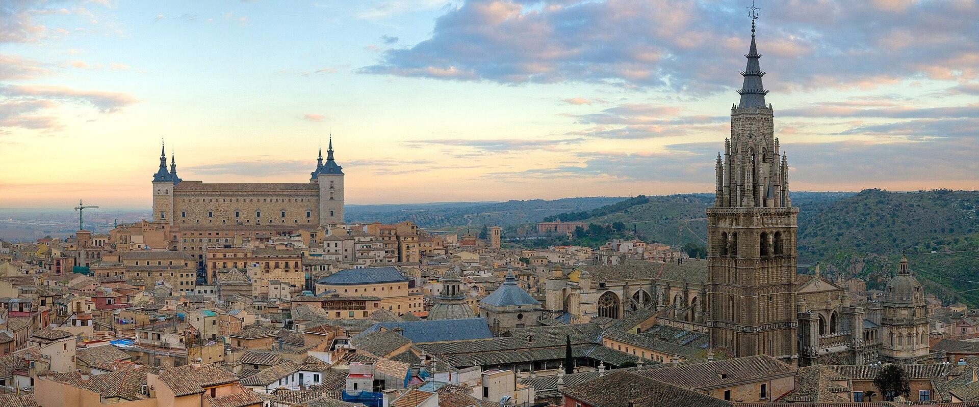 A panoramic view of the historic city of Toledo, Spain, featuring the Alcázar on the left and the bell tower of the Toledo Cathedral on the right.