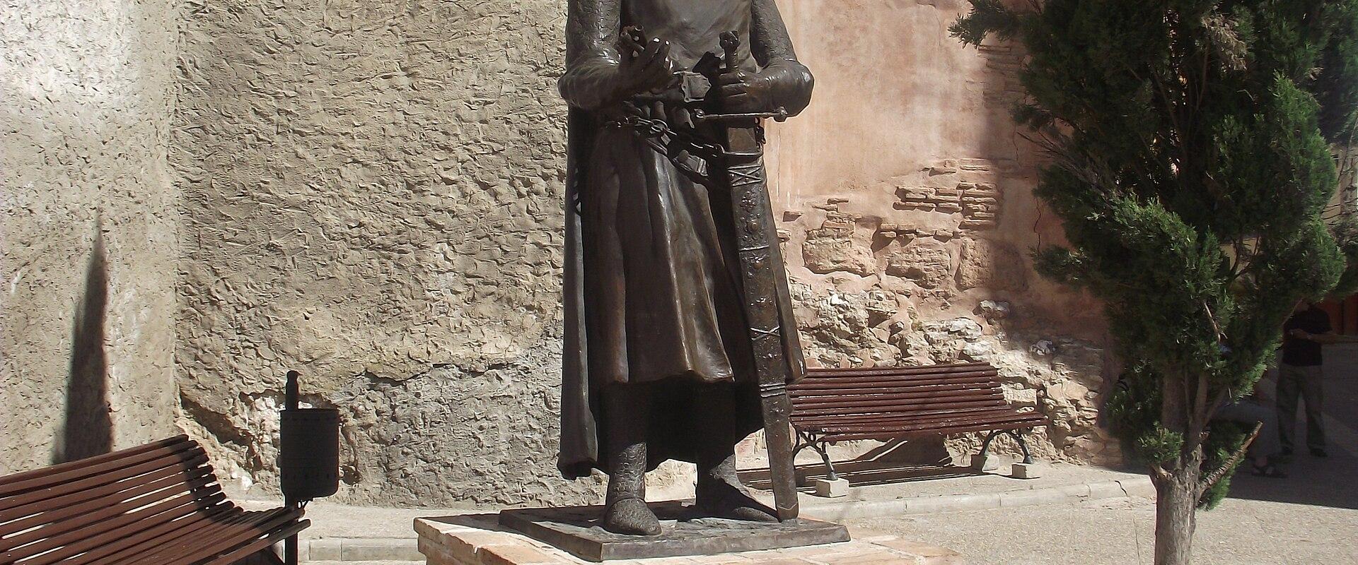 A bronze statue of a crowned medieval king standing on a brick pedestal in a paved plaza, with a plaque reading "ALFONSO I EL BATALLADOR" and "CONQUISTO CALATAYUD EN EL AÑO 1120".