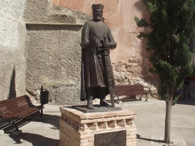 A bronze statue of a crowned medieval king standing on a brick pedestal in a paved plaza, with a plaque reading "ALFONSO I EL BATALLADOR" and "CONQUISTO CALATAYUD EN EL AÑO 1120".