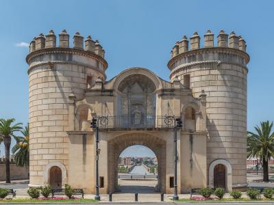 The image shows the Puerta de Palmas, a monumental city gate with two large cylindrical towers and a central archway, located in Badajoz, Spain.