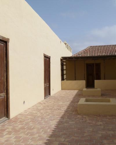 A sunlit interior courtyard of a traditional Canarian-style building with stucco walls, wooden doors, terracotta tile flooring, and two rectangular stone planters or water basins in the center.