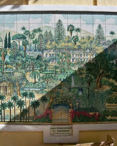 A large ceramic tile mural depicting a landscape with palm trees, a mansion, and a temple, mounted on a yellow wall with a small plaque below it.