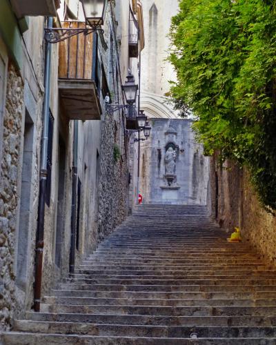 A long, steep stone staircase ascending between old buildings, leading to a statue of a religious figure set into a niche at the top, with a large church facade visible in the background.
