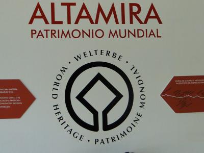 A white wall display featuring the large red text "ALTAMIRA PATRIMONIO MUNDIAL" above a circular UNESCO World Heritage logo, flanked by two red informational plaques.