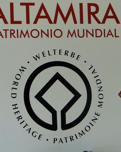 A white wall display featuring the large red text "ALTAMIRA PATRIMONIO MUNDIAL" above a circular UNESCO World Heritage logo, flanked by two red informational plaques.