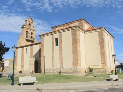 A beige and brick church with a bell tower, set in a town square with benches and lampposts under a blue sky.