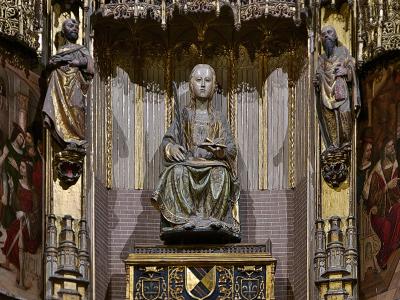 A close-up view of an ornate, gilded Gothic-style altarpiece featuring a central seated statue of a female saint holding a book, flanked by standing figures and intricate architectural details.