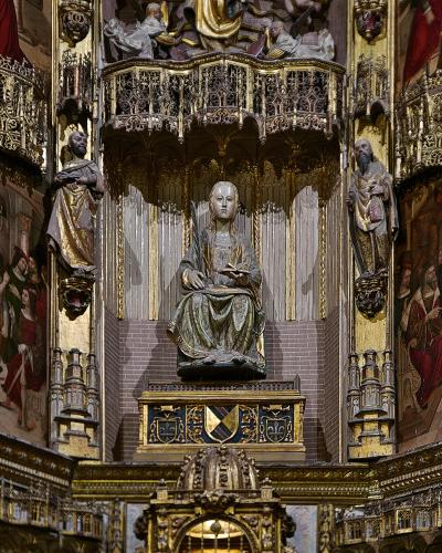 A close-up view of an ornate, gilded Gothic-style altarpiece featuring a central seated statue of a female saint holding a book, flanked by standing figures and intricate architectural details.