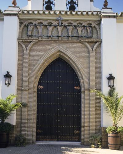 The image shows the facade of a white-walled chapel with a horseshoe arch doorway, brick detailing, and a sign reading "ERMITA SIGLO XVIII" above the entrance, along with a decorative "FELIZ 2000" banner.