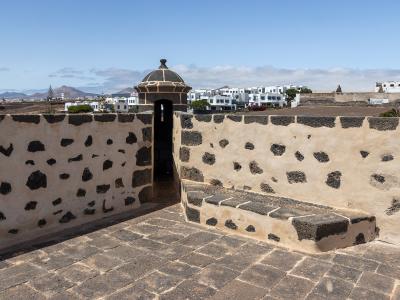A stone terrace with a distinctive sentry box (garita) featuring a domed roof, overlooking white buildings and volcanic terrain under a blue sky.