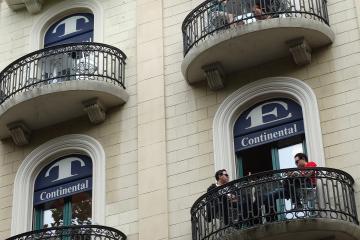 A low-angle shot of a cream-colored building facade featuring arched windows with blue signs reading "Continental" and people sitting on curved iron balconies.
