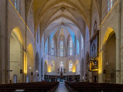 The interior of a large stone church showing the main nave, vaulted ceilings, stained glass windows, and an organ on the right side.