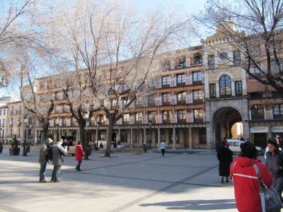 A wide, paved public square lined with multi-story buildings featuring arcades and balconies, with bare trees and pedestrians.