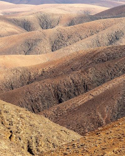 A landscape photograph showing rolling, arid hills with eroded gullies and sparse vegetation, characteristic of a volcanic desert environment.