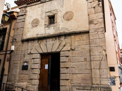 The image shows the facade of a small, stone-walled chapel with a terracotta tiled roof, a bell in a small bell tower, and a plaque on the wall to the left of the entrance that reads "Capilla de la Soledad".