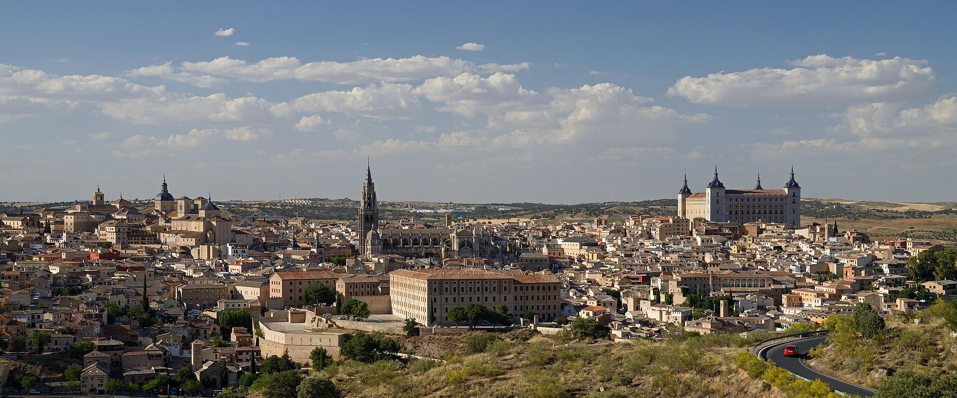 A panoramic view of the historic city of Toledo, Spain, featuring the Alcázar on the right and the spire of the Cathedral in the center.