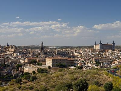 A panoramic view of the historic city of Toledo, Spain, featuring the Alcázar on the right and the spire of the Cathedral in the center.