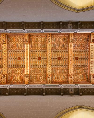 An interior view looking up at an ornate, coffered wooden ceiling (techumbre) with geometric and floral patterns, supported by decorative beams, inside a large cathedral-like space.