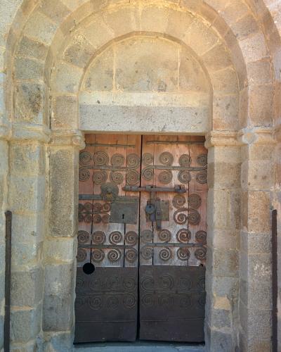 A close-up of a Romanesque stone doorway with a wooden double door adorned with spiral ironwork, set within a rounded archway.