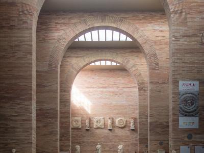 The image shows the interior of a modern museum with distinctive red brick arches, skylights, and Roman sculptures on display.