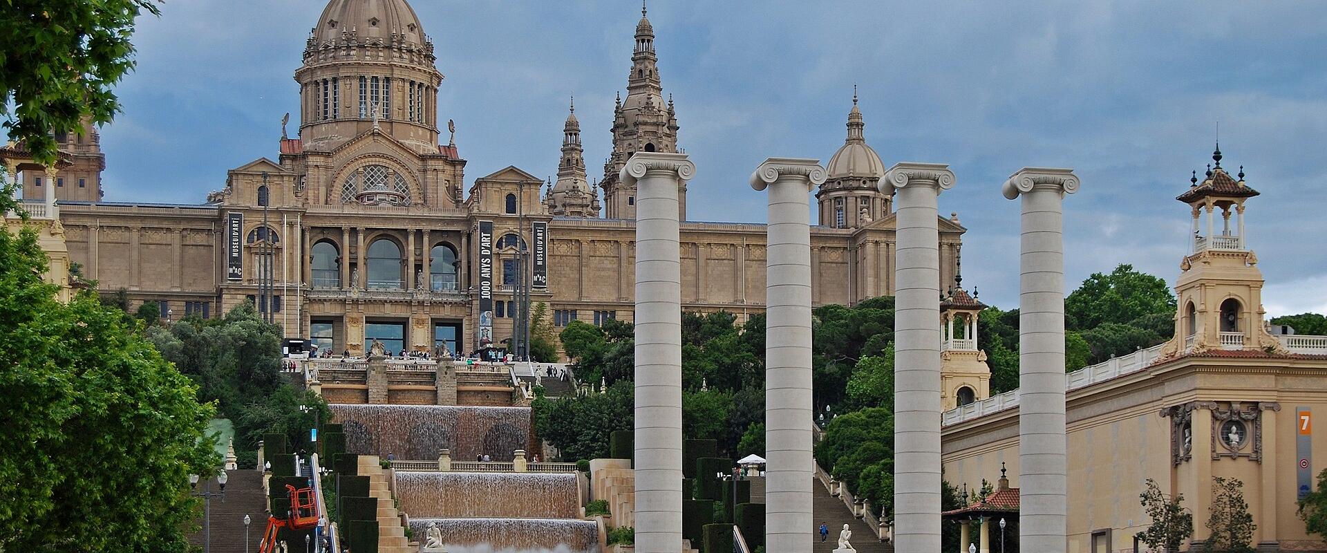 A view from a tiled terrace looking through a colonnade towards the large central dome and facade of the Palau Nacional.