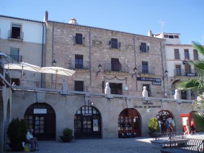 A stone building with arched ground-floor entrances, a terrace with umbrellas, and signage reading "Casa la cadena" and "Turismo Oficina de Información".