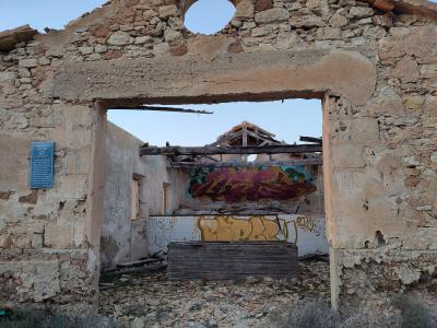 A ruined stone building with a large doorway, graffiti-covered interior walls, and a blue informational plaque mounted on the left wall.