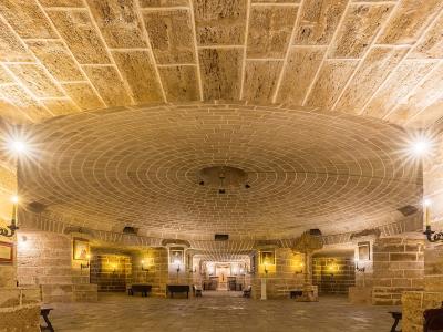 The image shows the interior of a stone crypt or underground chapel with a large central dome, arched ceilings, religious paintings, and candle sconces.