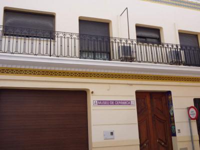 A cream-colored building facade with decorative ceramic tile bands, a brown garage door, a wooden entrance door, and a sign reading "MUSEU DE CERÀMICA" next to the door.