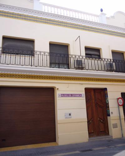A cream-colored building facade with decorative ceramic tile bands, a brown garage door, a wooden entrance door, and a sign reading "MUSEU DE CERÀMICA" next to the door.