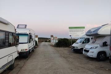 A paved path lined with parked camper vans and motorhomes, featuring a large informational sign on the right side.