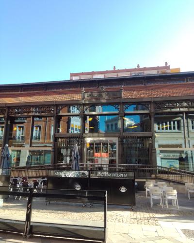 The image shows the exterior of a large, historic iron-and-glass market building with a terracotta-tiled roof, featuring outdoor seating areas and a prominent sign reading "MERCADO DEL VAL" above the entrance.
