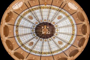 A fisheye photograph looking directly up at the ornate, circular stained-glass dome of the Palacio de Correos y Telégrafos in Valencia, Spain.