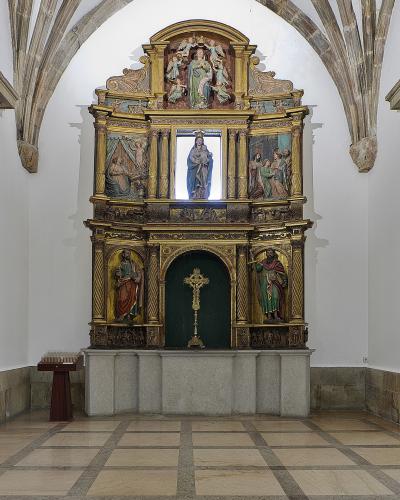 The image shows an ornate, gilded wooden altarpiece (retablo) with multiple painted panels and sculptures, situated within a stone-arched chapel or side chapel of a church.